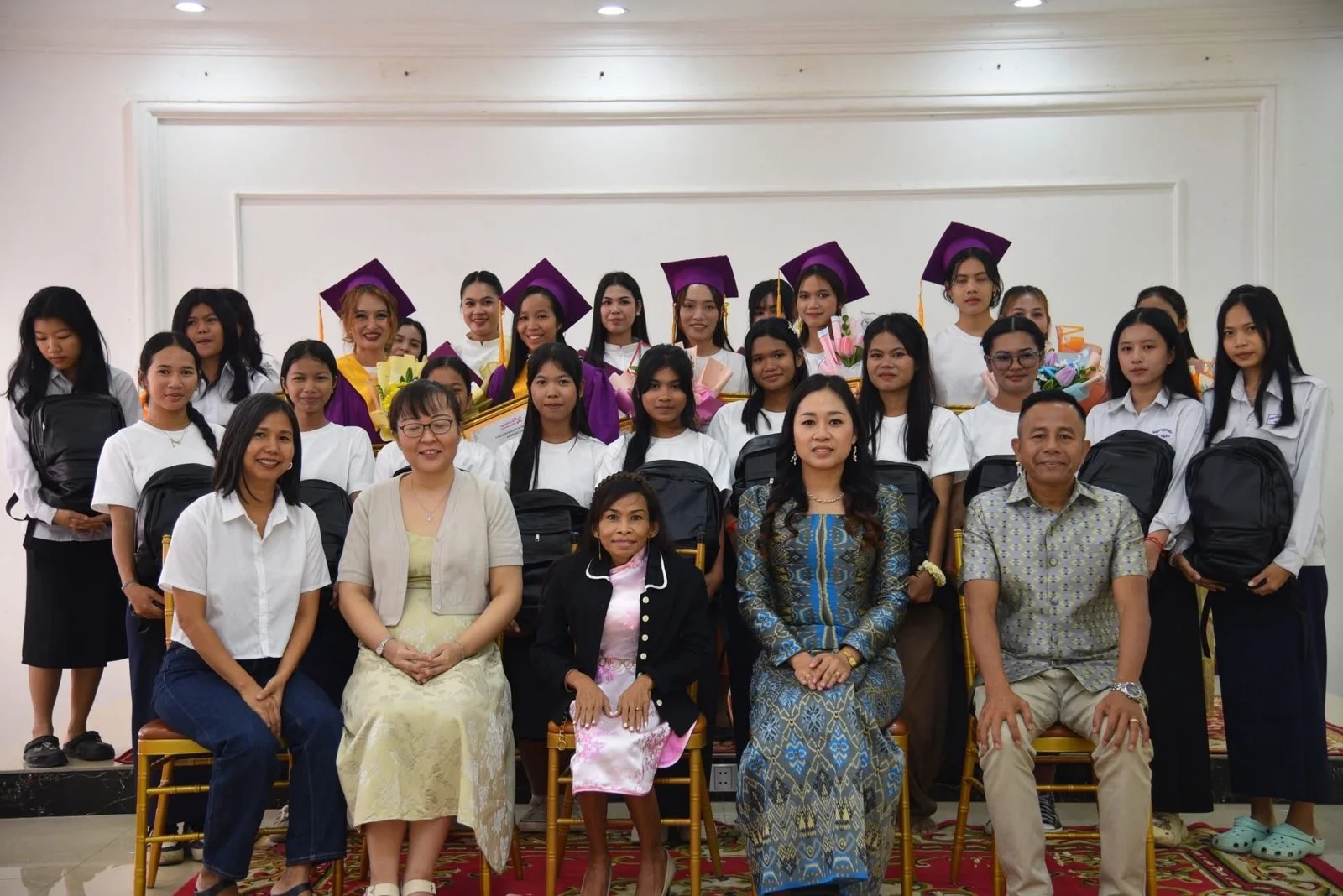 Naleng Real seated with graduating students in caps and gowns at a Precious Women graduation