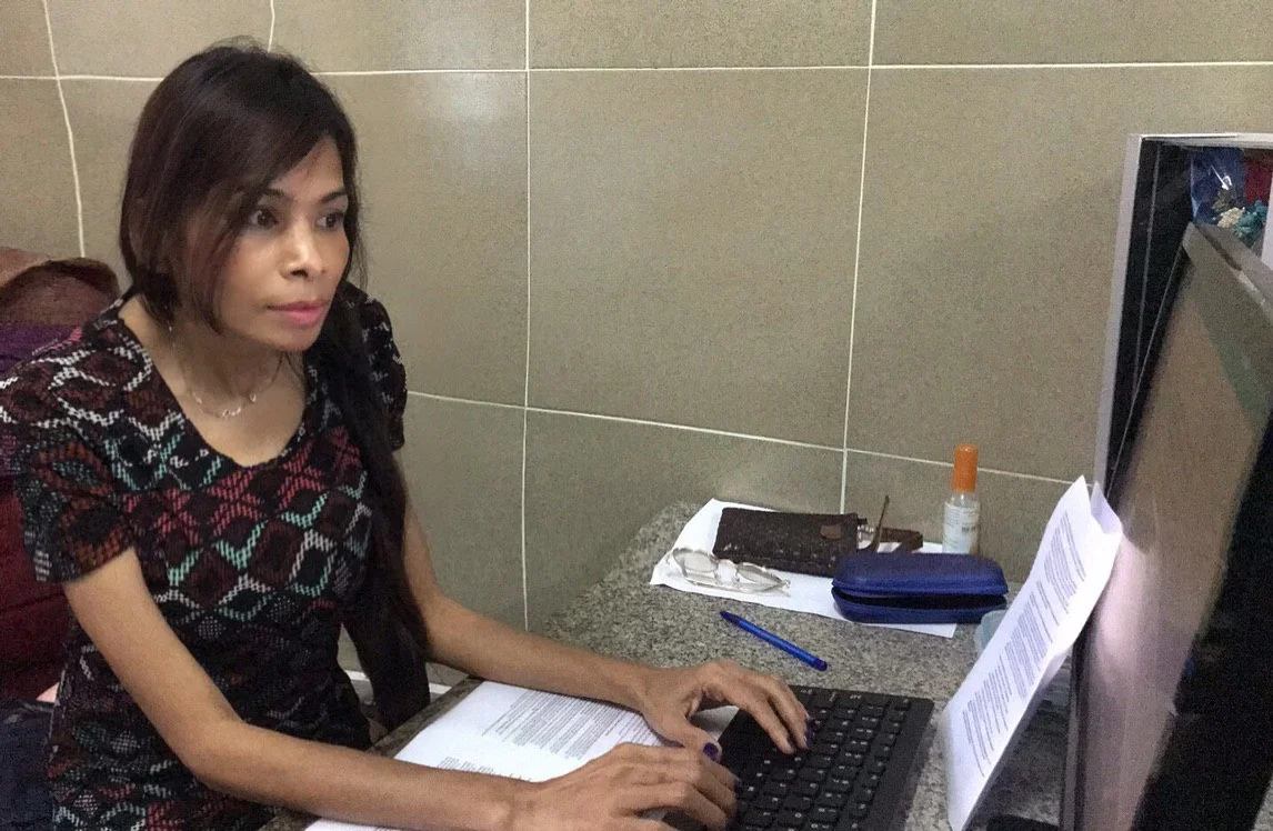 Naleng Real typing at a computer with a printed manuscript beside the keyboard